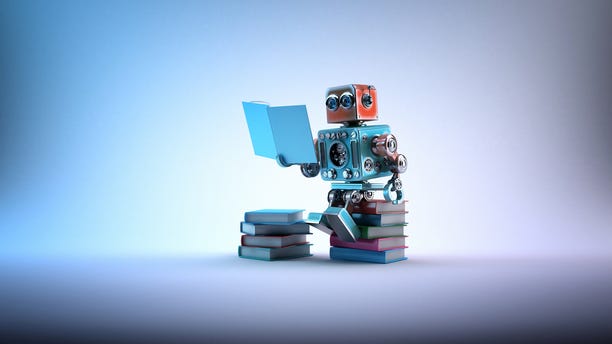 A toy robot reads a tiny book, while sitting atop a pile of tiny books.